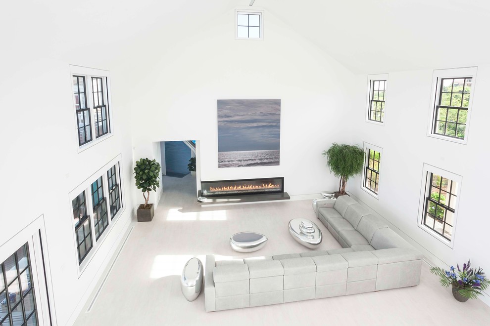 Diseño de salón abierto moderno grande sin televisor con paredes blancas, suelo de madera clara, chimenea lineal y marco de chimenea de yeso