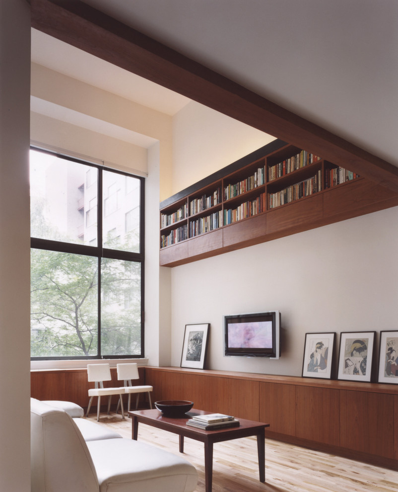 Minimalist loft-style light wood floor living room library photo in New York with white walls and a wall-mounted tv