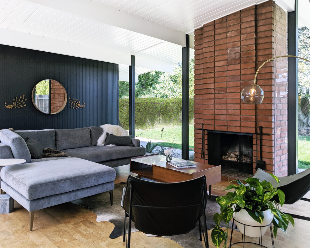 Cette image montre un salon vintage ouvert avec un mur noir, un sol en bois brun, une cheminée standard, un manteau de cheminée en brique et un sol marron.