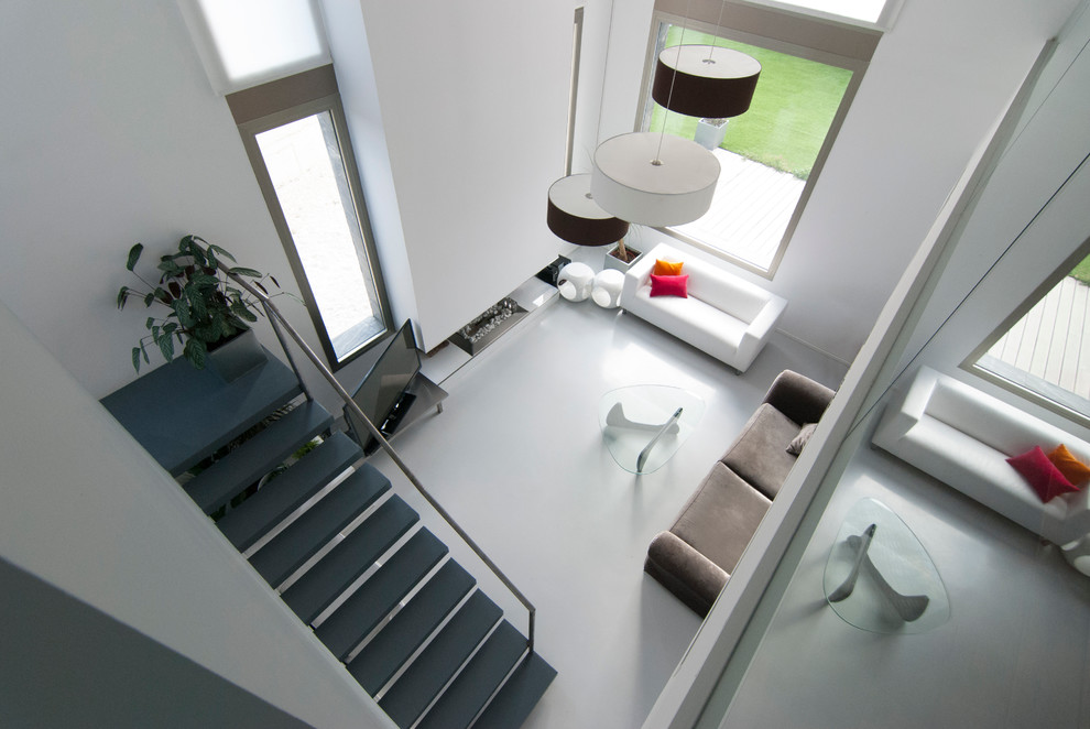 Modelo de salón para visitas abierto minimalista con paredes blancas, suelo de cemento, chimenea lineal, marco de chimenea de metal y televisor independiente
