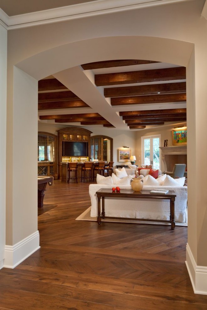 Exemple d'un salon sud-ouest américain de taille moyenne et ouvert avec un mur beige, un sol en bois brun, une cheminée standard, un manteau de cheminée en plâtre et un sol marron.