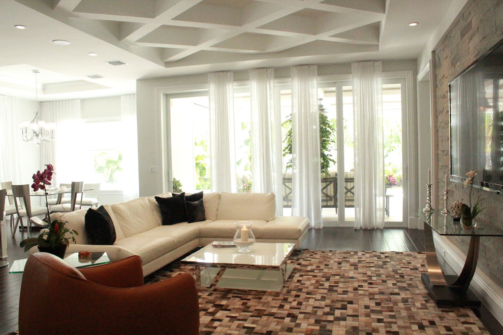 На фото: большая парадная, открытая гостиная комната в стиле неоклассика (современная классика) с белыми стенами, темным паркетным полом, телевизором на стене и коричневым полом без камина