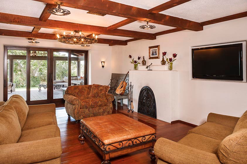 Mittelgroßes, Abgetrenntes Mediterranes Wohnzimmer mit weißer Wandfarbe, braunem Holzboden, Kamin, verputzter Kaminumrandung und Multimediawand in San Diego
