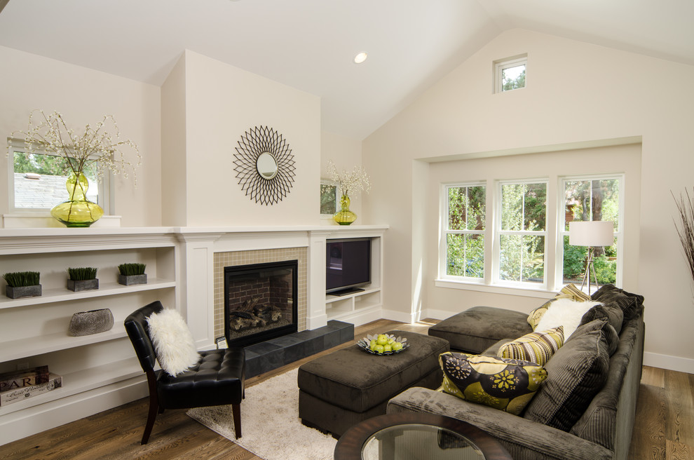 На фото: гостиная комната в современном стиле с бежевыми стенами, стандартным камином, фасадом камина из плитки, отдельно стоящим телевизором и коричневым диваном