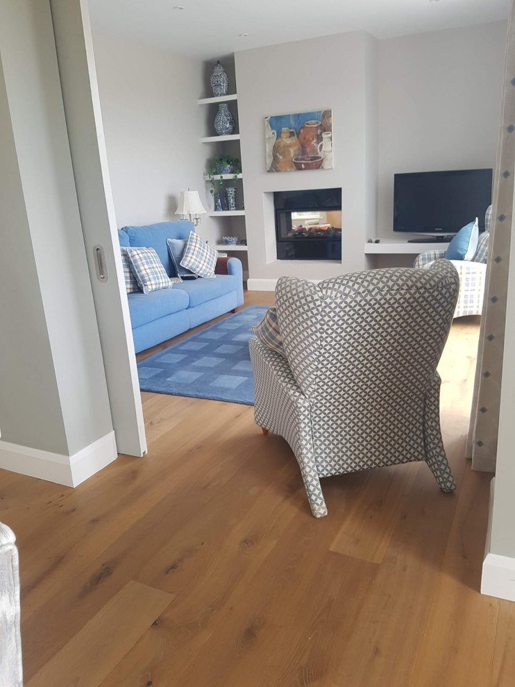 Geräumiges, Offenes Uriges Wohnzimmer mit grauer Wandfarbe, braunem Holzboden, Tunnelkamin und freistehendem TV in Cork