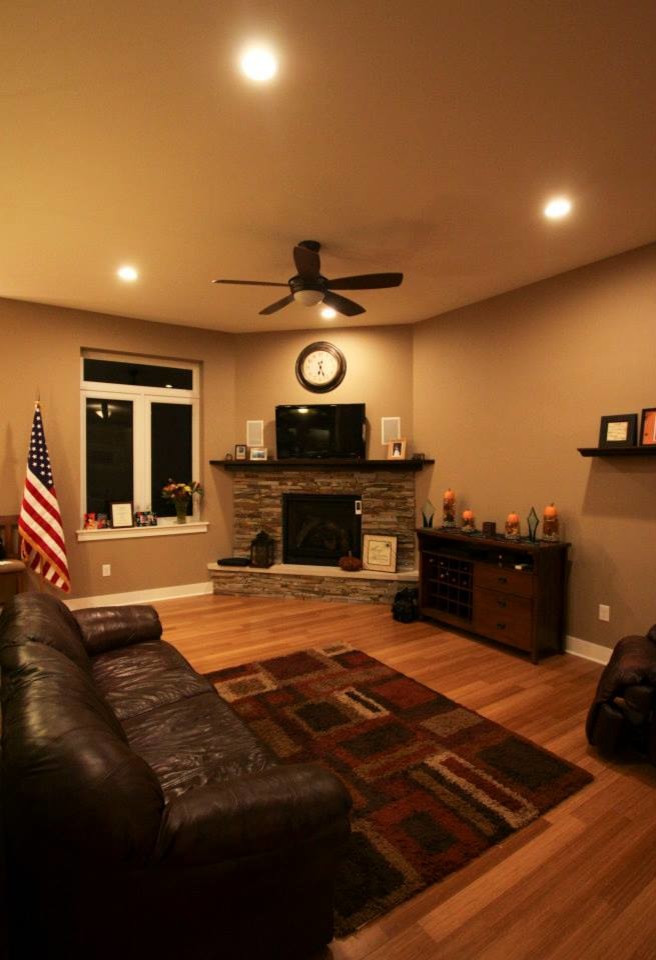 Foto de salón abierto tradicional renovado de tamaño medio con paredes beige, suelo de madera en tonos medios, chimenea de esquina, marco de chimenea de piedra y televisor colgado en la pared