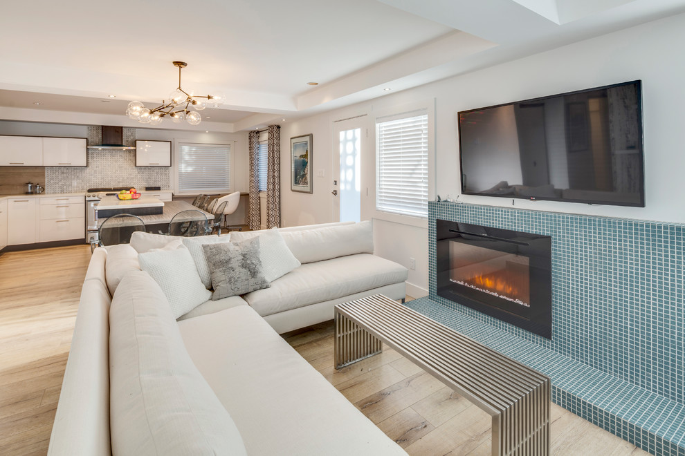 バンクーバーにある低価格の小さなコンテンポラリースタイルのおしゃれなLDK (白い壁、ラミネートの床、タイルの暖炉まわり、標準型暖炉、壁掛け型テレビ、茶色い床) の写真