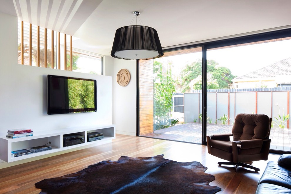 На фото: изолированная гостиная комната среднего размера в современном стиле с белыми стенами, телевизором на стене и паркетным полом среднего тона с