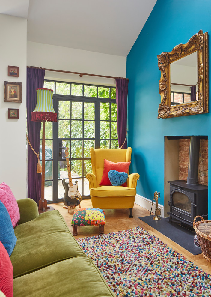 Bohemian living room in Oxfordshire with blue walls, light hardwood flooring and a wood burning stove.