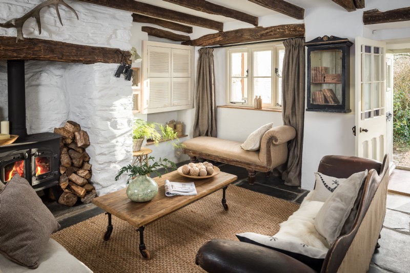 Country Wohnzimmer mit weißer Wandfarbe, Schieferboden, Kaminofen, Kaminumrandung aus Stein und verstecktem TV in Cornwall