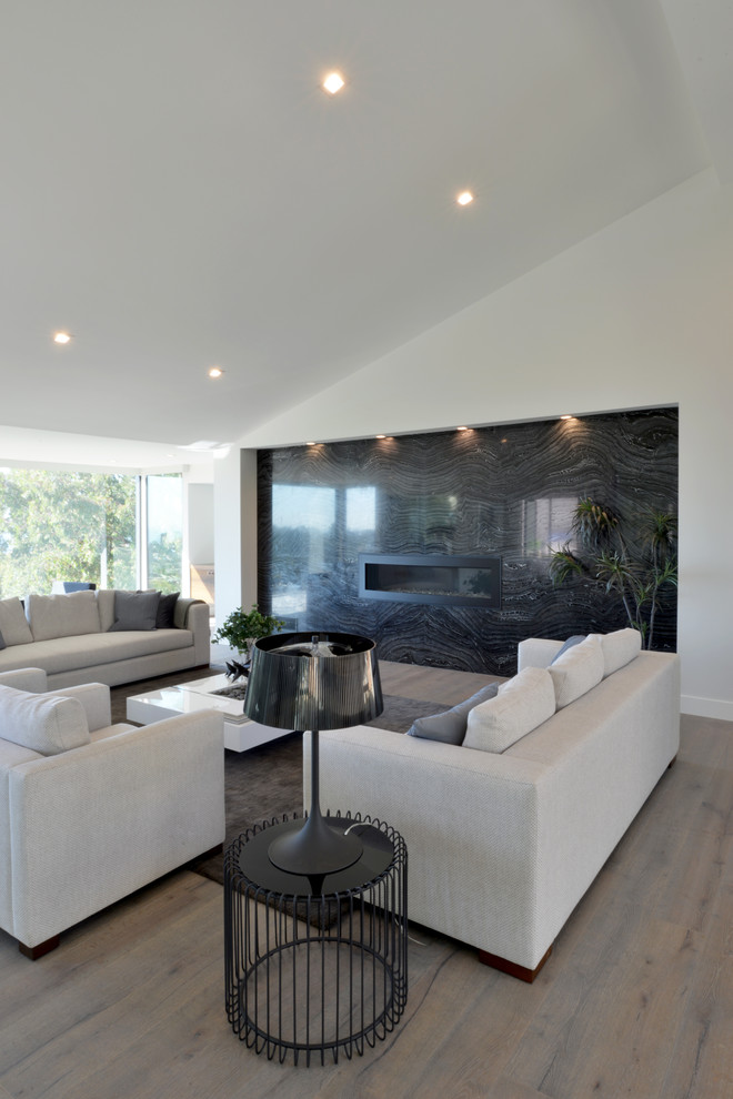 This is an example of an expansive modern enclosed living room in San Diego with a home bar, white walls, a ribbon fireplace, a stone fireplace surround, no tv and light hardwood flooring.