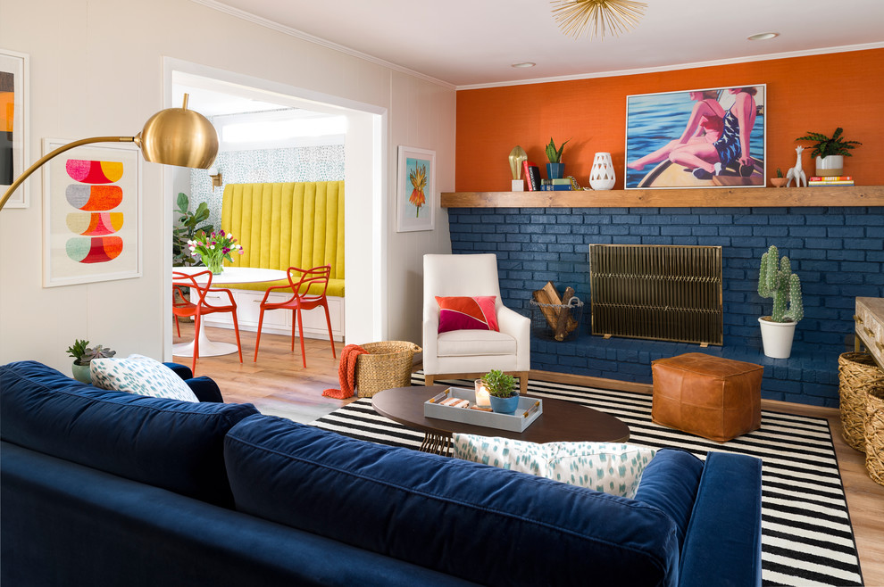 Источник вдохновения для домашнего уюта: изолированная гостиная комната в стиле фьюжн с светлым паркетным полом, стандартным камином, фасадом камина из кирпича, оранжевыми стенами и синим диваном без телевизора