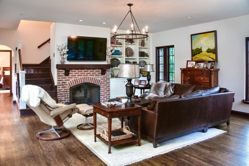 Medium sized classic open plan living room with white walls, dark hardwood flooring, a standard fireplace, a brick fireplace surround, a wall mounted tv and brown floors.