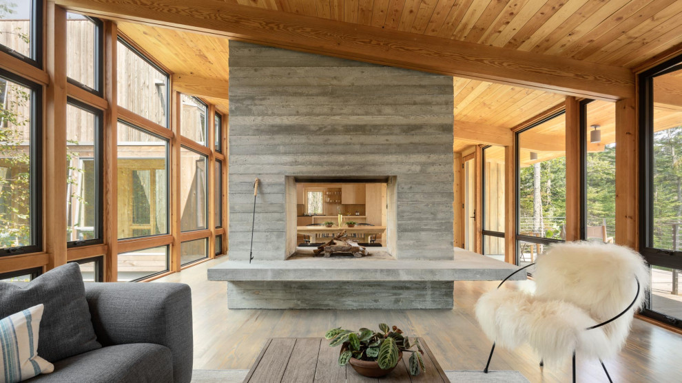 Photo of a large modern enclosed living room in Portland Maine with brown walls, medium hardwood flooring, a two-sided fireplace, a concrete fireplace surround and grey floors.