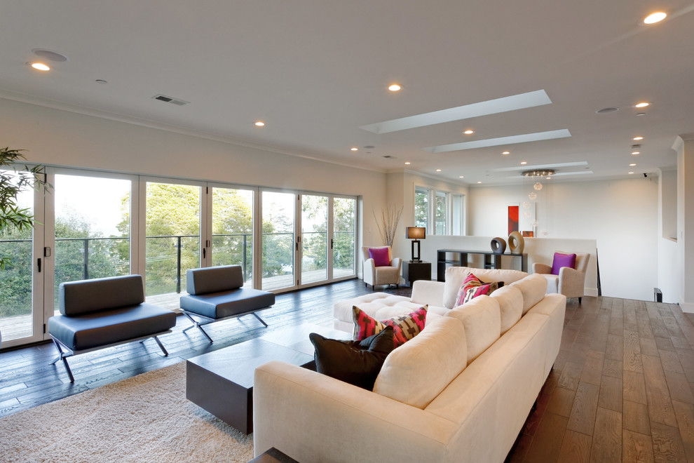 Cette image montre un grand salon minimaliste avec un mur blanc, un sol marron et parquet foncé.