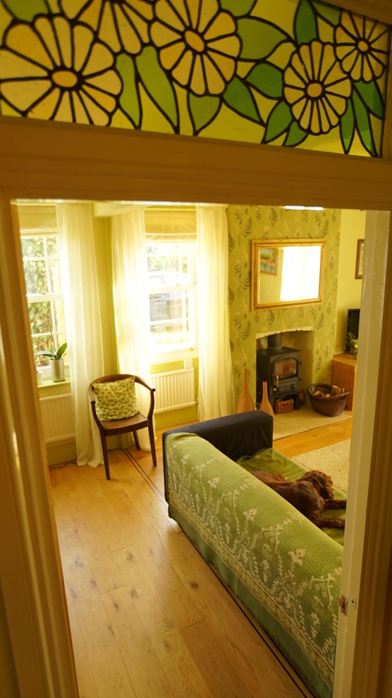 Mittelgroßes, Abgetrenntes Landhaus Wohnzimmer mit grüner Wandfarbe, braunem Holzboden, Kaminofen und Kaminumrandung aus Backstein in Sonstige