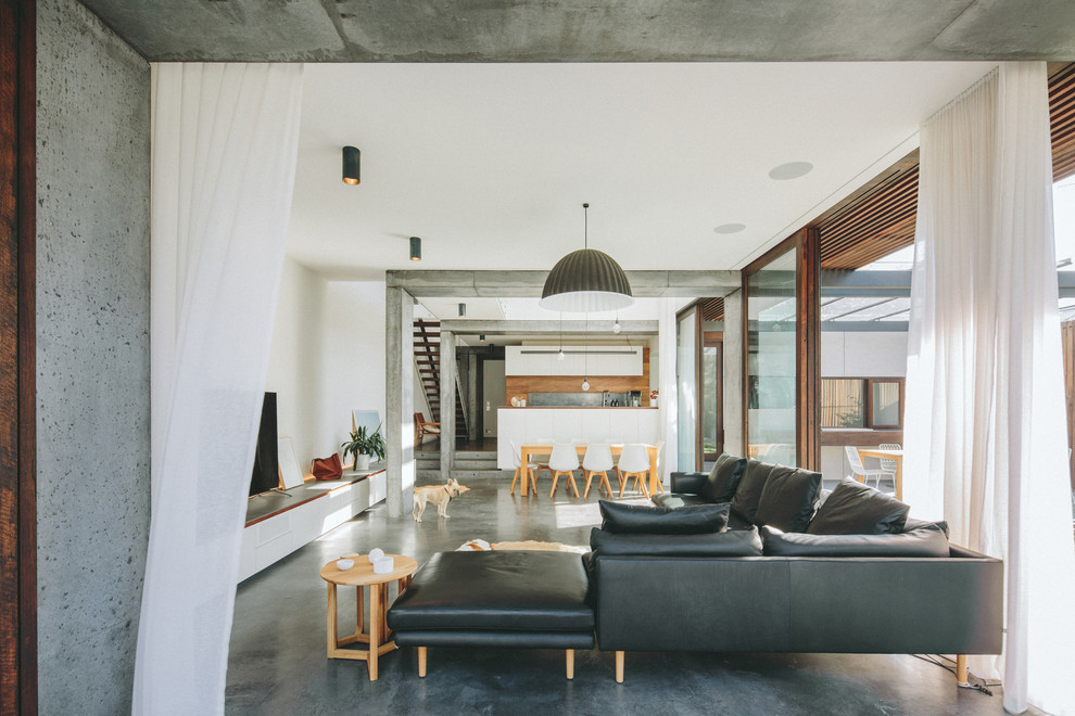Diseño de salón abierto contemporáneo con paredes blancas, suelo de cemento, televisor independiente y suelo gris