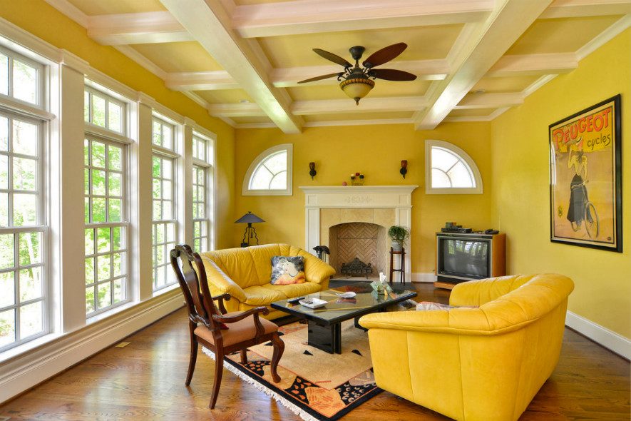 Cette image montre un salon avec une salle de réception, un mur jaune, un sol en bois brun, une cheminée standard, un manteau de cheminée en plâtre et un téléviseur indépendant.
