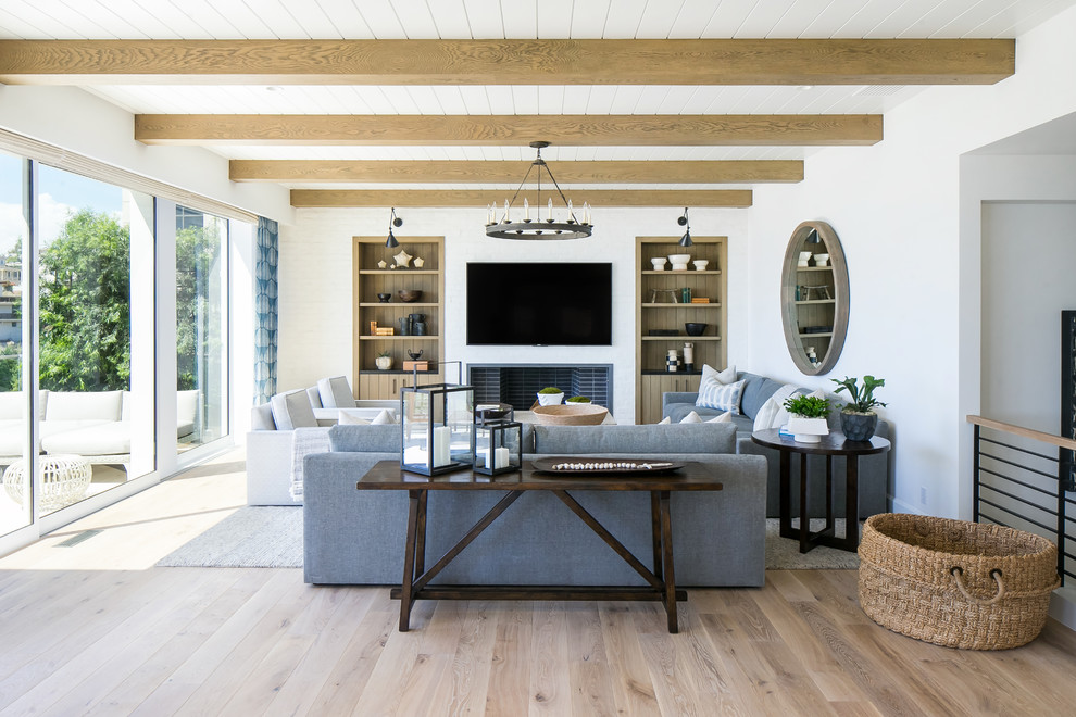 Imagen de salón costero con paredes blancas, suelo de madera clara, todas las chimeneas, televisor colgado en la pared y suelo beige