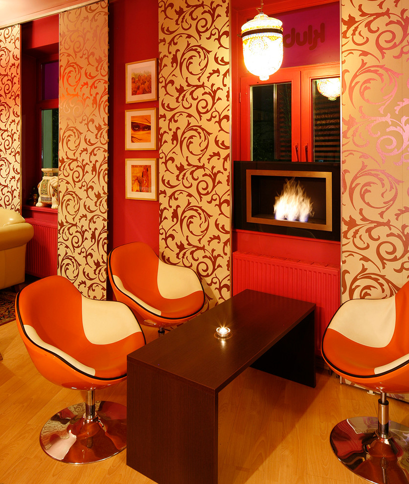 На фото: гостиная комната среднего размера в восточном стиле с красными стенами, светлым паркетным полом, горизонтальным камином и фасадом камина из металла без телевизора