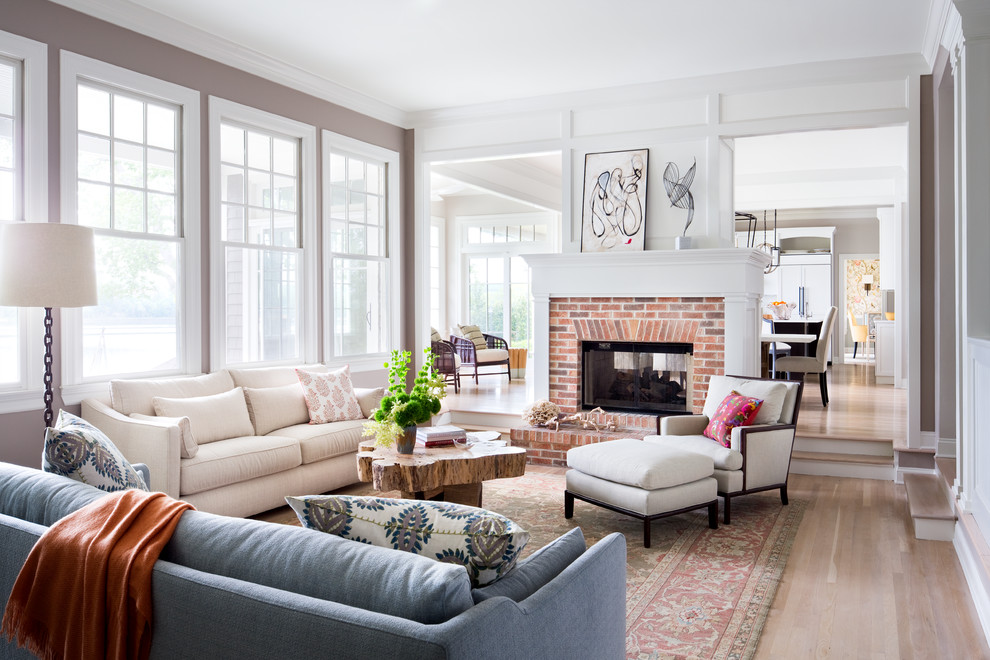 This is an example of a large classic formal open plan living room in New York with light hardwood flooring, a two-sided fireplace, a brick fireplace surround, white walls and beige floors.