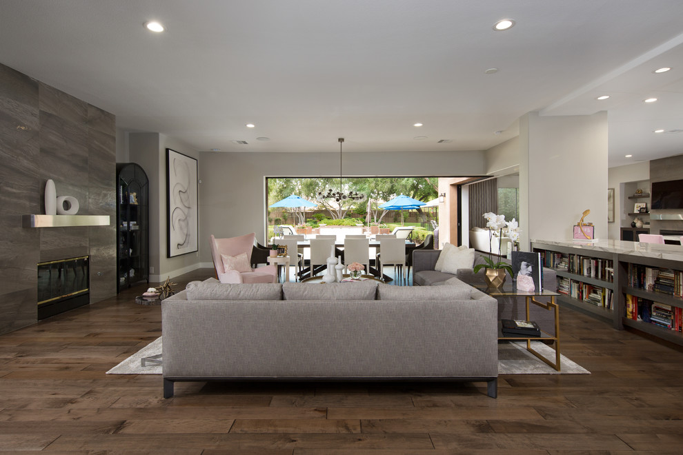 This is an example of a large contemporary open plan living room in Las Vegas with grey walls, medium hardwood flooring, a standard fireplace, a tiled fireplace surround and brown floors.