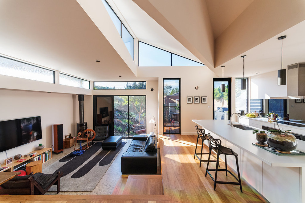 Modernes Wohnzimmer mit beiger Wandfarbe, hellem Holzboden, Kaminofen, Kaminumrandung aus Metall, TV-Wand und beigem Boden in Melbourne