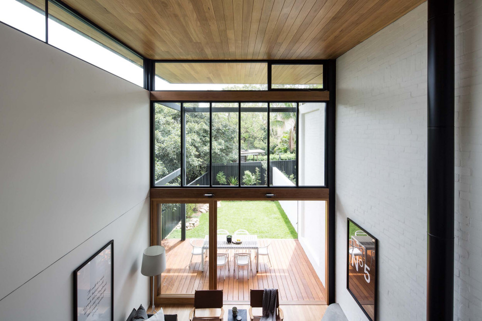 Modern inredning av ett mellanstort loftrum, med vita väggar, mellanmörkt trägolv, en standard öppen spis och en spiselkrans i tegelsten