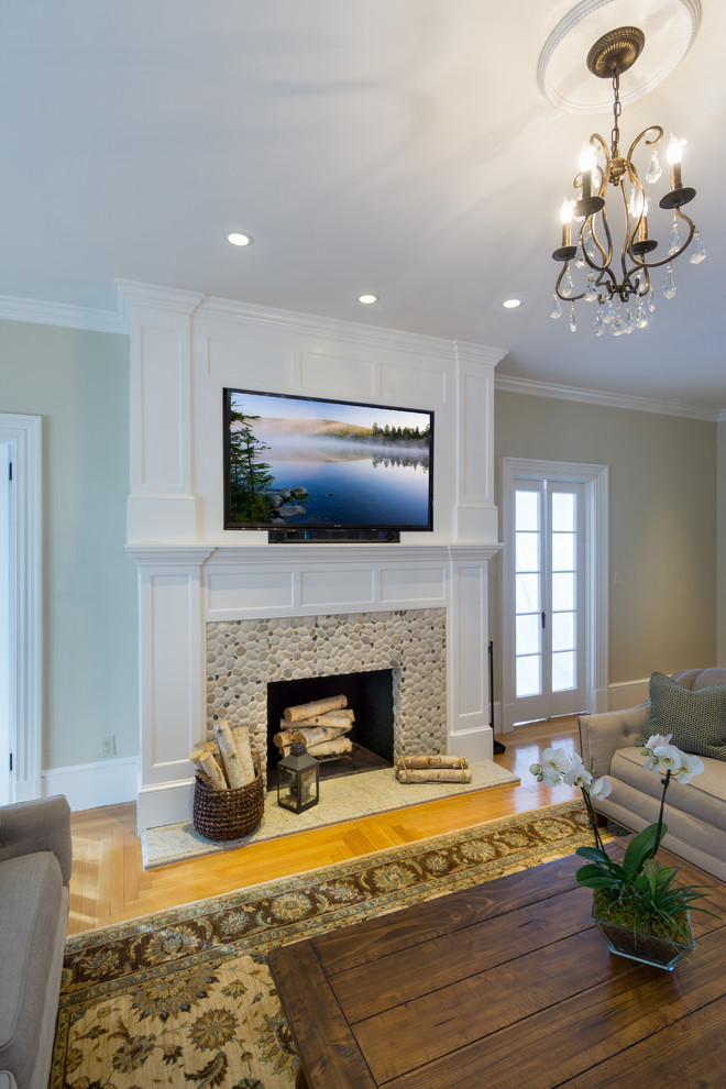 Imagen de salón cerrado clásico grande con televisor colgado en la pared, paredes beige, suelo de madera clara, todas las chimeneas y marco de chimenea de madera