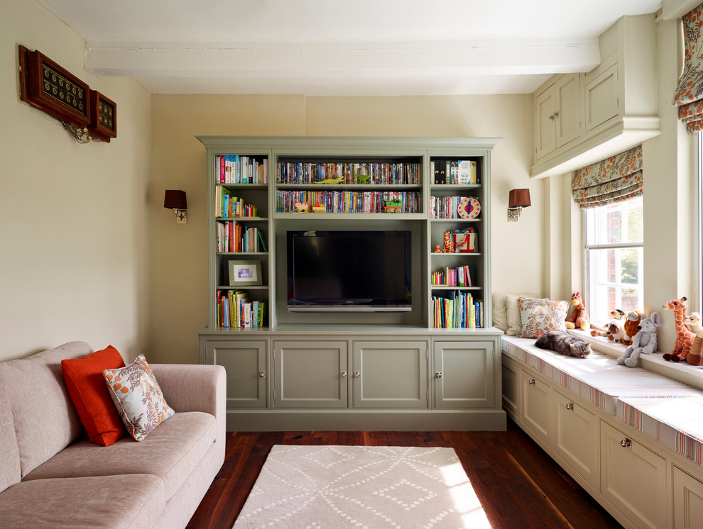 Modelo de biblioteca en casa tradicional de tamaño medio con paredes beige, suelo de madera en tonos medios y televisor independiente