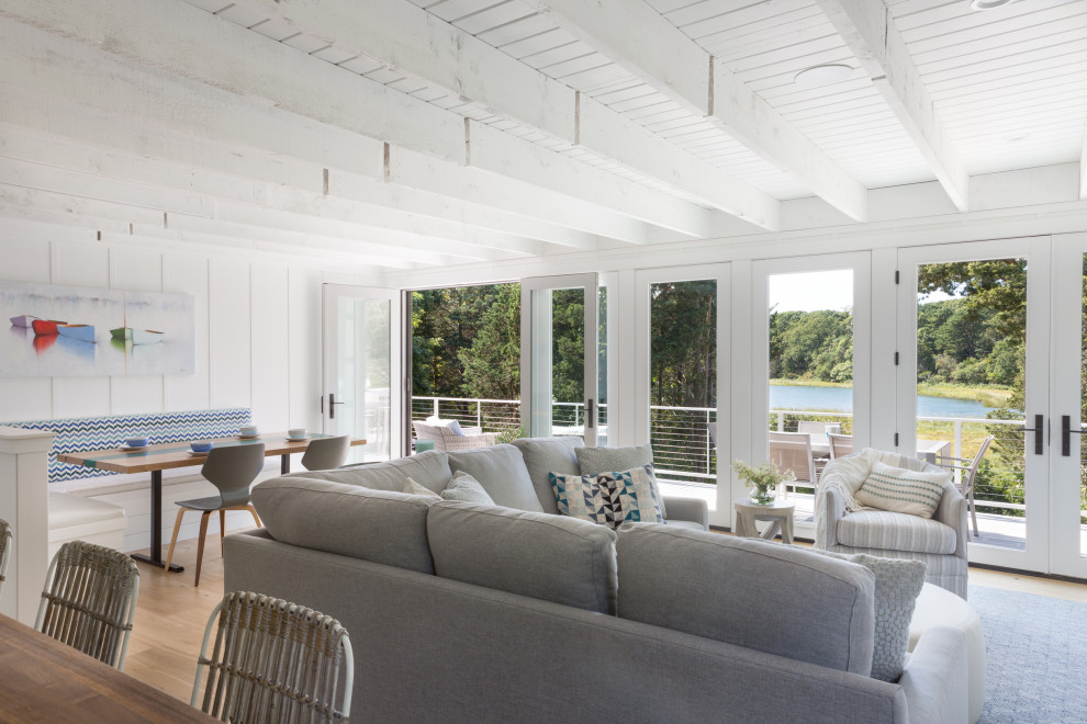 Immagine di un soggiorno costiero aperto con pareti bianche, parquet chiaro, pavimento beige, travi a vista e soffitto in perlinato