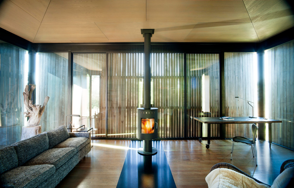Foto di un piccolo soggiorno moderno aperto con pareti marroni, pavimento in legno massello medio, stufa a legna e cornice del camino in metallo