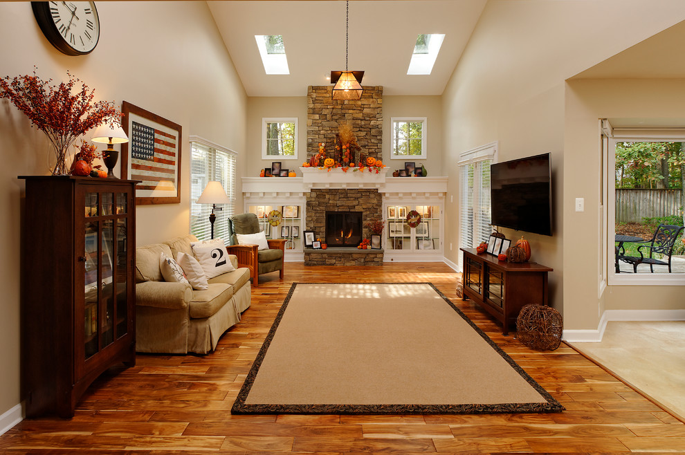Example of a mid-sized classic enclosed medium tone wood floor and brown floor living room design in DC Metro with beige walls, a standard fireplace, a stone fireplace and a wall-mounted tv