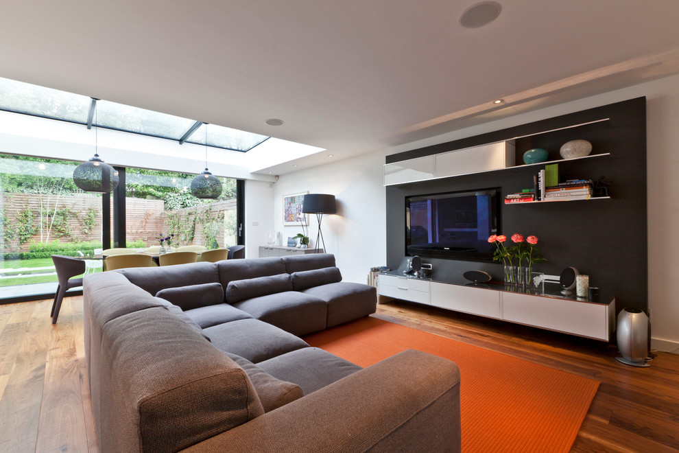 Mittelgroßes, Offenes Modernes Wohnzimmer mit weißer Wandfarbe, braunem Holzboden und Multimediawand in London