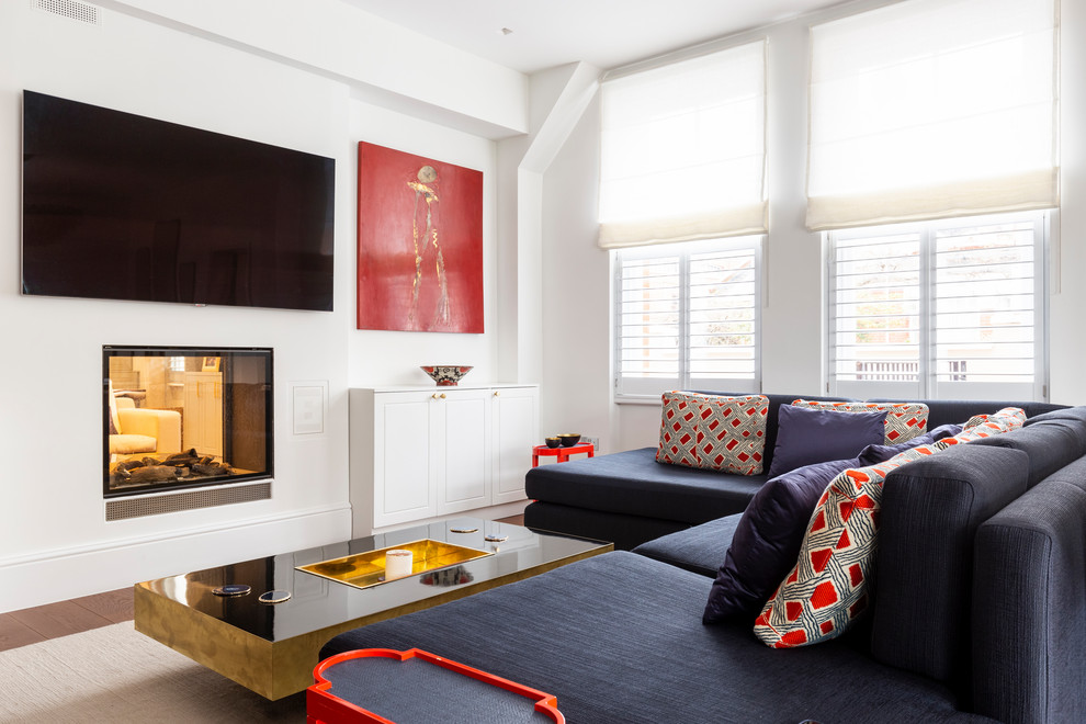 Foto di un soggiorno minimal aperto con pareti bianche, pavimento in legno massello medio, camino bifacciale, TV a parete e pavimento marrone