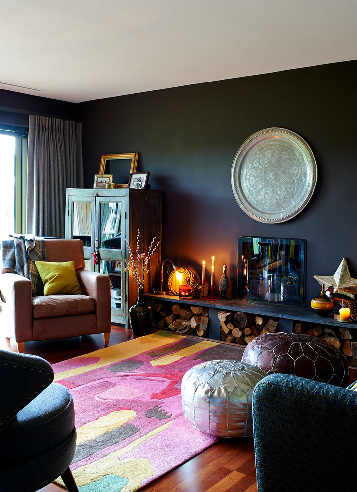 На фото: гостиная комната в стиле фьюжн с черными стенами, паркетным полом среднего тона, стандартным камином и фасадом камина из металла