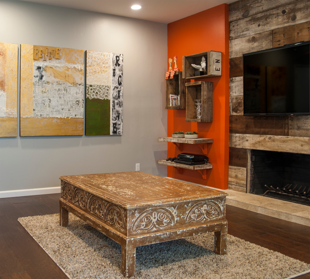 На фото: изолированная гостиная комната среднего размера в стиле рустика с оранжевыми стенами, темным паркетным полом, стандартным камином, фасадом камина из дерева и телевизором на стене с