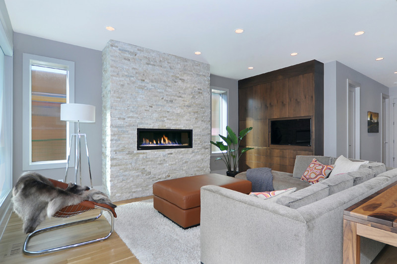 Modernes Wohnzimmer mit grauer Wandfarbe, hellem Holzboden, Gaskamin, Kaminumrandung aus Stein und Multimediawand in Calgary