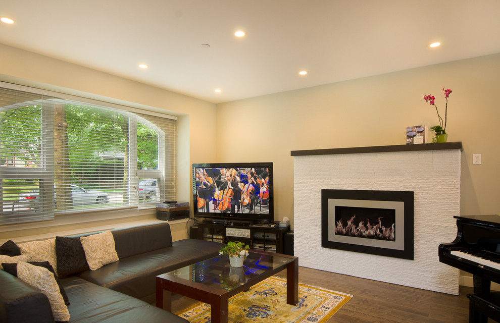 バンクーバーにある中くらいなトランジショナルスタイルのおしゃれなLDK (黄色い壁、無垢フローリング、標準型暖炉、漆喰の暖炉まわり、据え置き型テレビ) の写真
