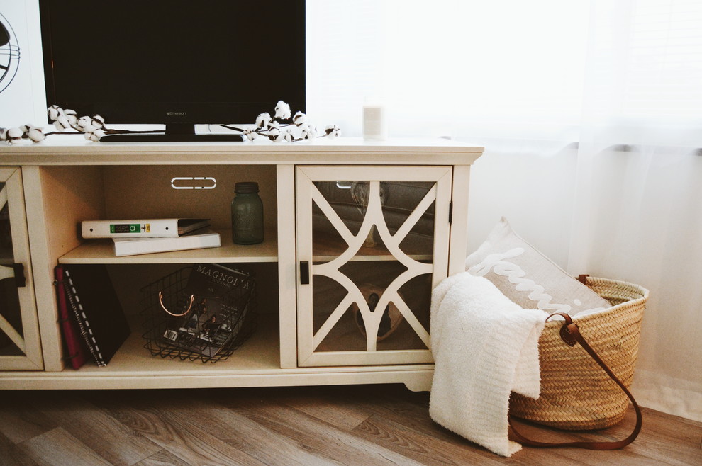 Modelo de salón cerrado campestre pequeño con paredes blancas, suelo de madera clara, televisor independiente y suelo marrón