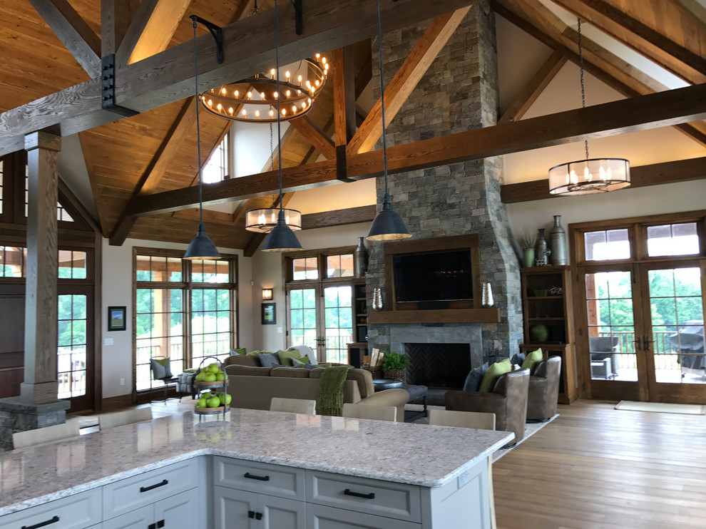 Large cottage loft-style medium tone wood floor and brown floor living room photo in Philadelphia with beige walls, a standard fireplace, a stone fireplace and a wall-mounted tv