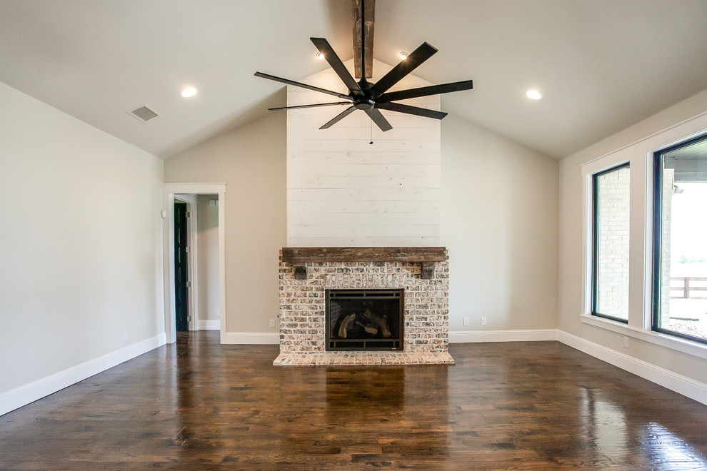 Inspiration for a large farmhouse open concept dark wood floor and brown floor living room remodel in Dallas with gray walls, a standard fireplace, a brick fireplace and a wall-mounted tv