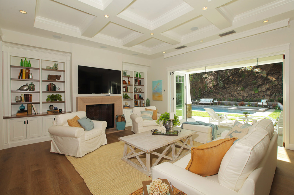 Großes, Offenes Landhaus Wohnzimmer mit beiger Wandfarbe, braunem Holzboden, Kamin, verputzter Kaminumrandung und TV-Wand in Los Angeles