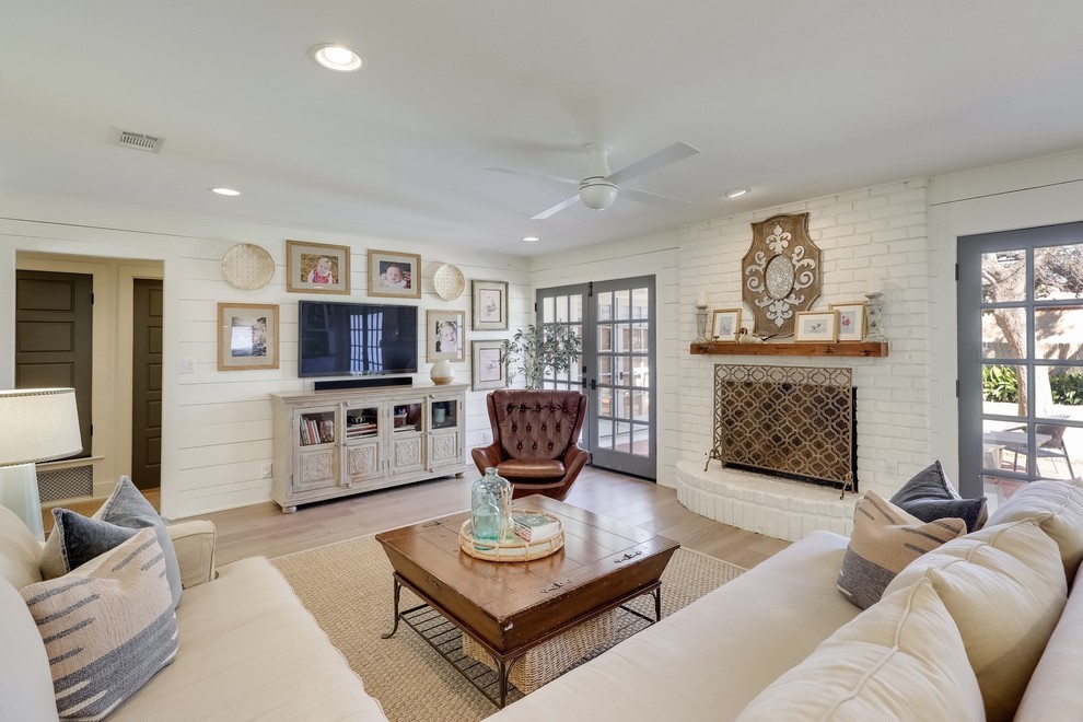Inspiration for a medium sized rural formal enclosed living room in Austin with light hardwood flooring, white walls, a standard fireplace, a brick fireplace surround, a wall mounted tv and beige floors.