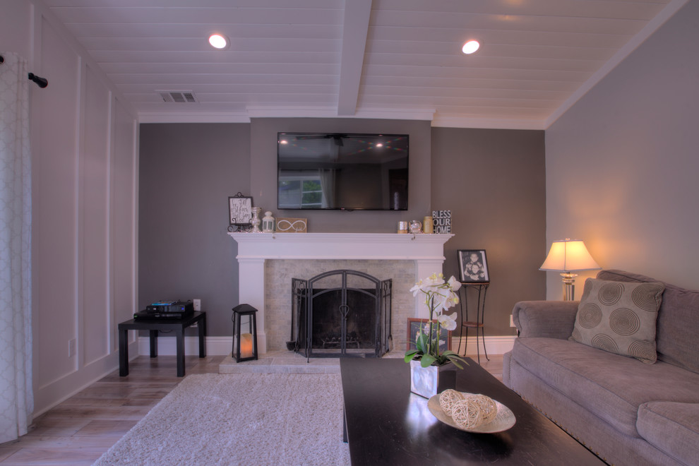 Inredning av ett lantligt mellanstort separat vardagsrum, med ett finrum, grå väggar, mellanmörkt trägolv, en standard öppen spis, en spiselkrans i sten, en väggmonterad TV och grått golv