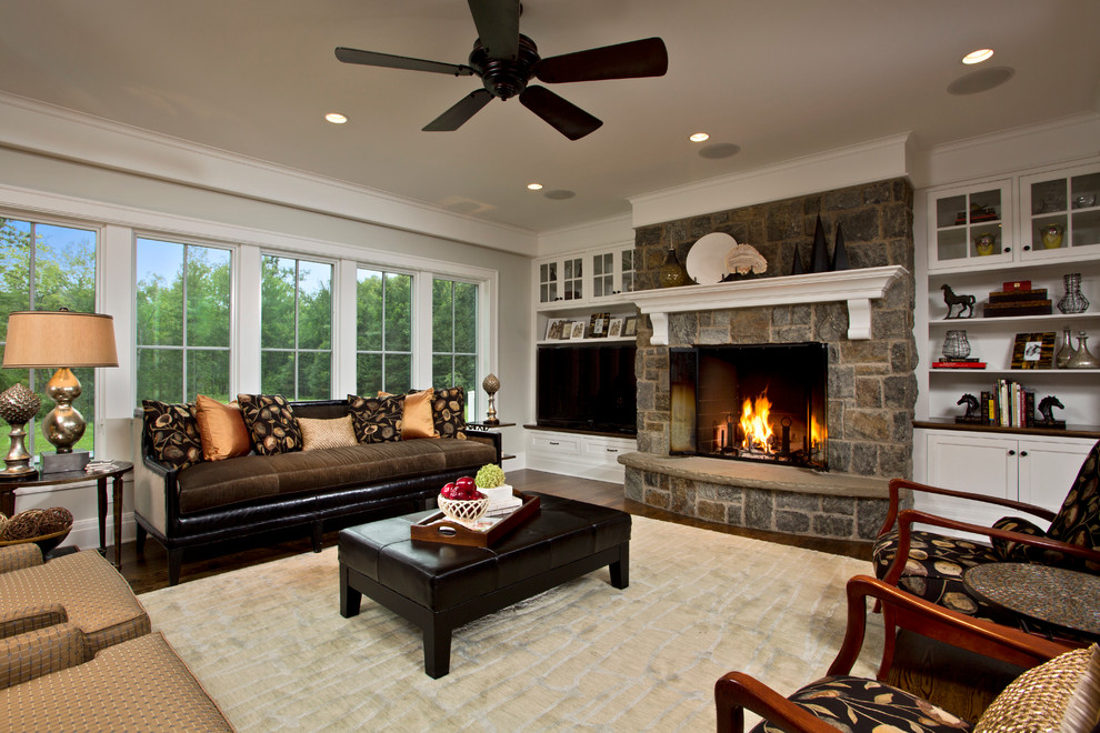Cette photo montre un grand salon nature ouvert avec un mur gris, un sol en bois brun, une cheminée standard, un manteau de cheminée en pierre et un téléviseur fixé au mur.