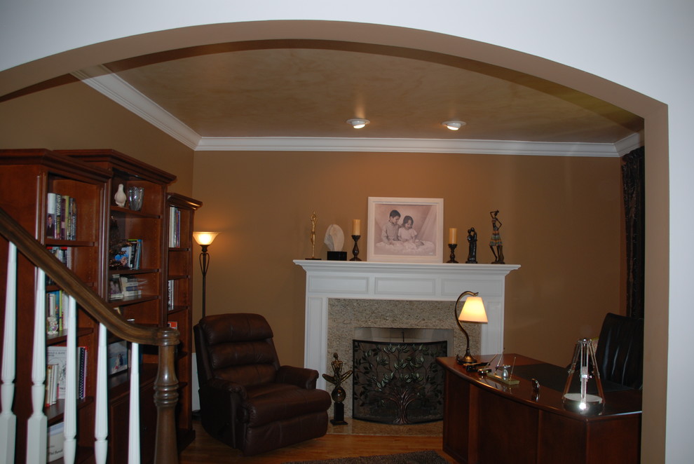 Ejemplo de biblioteca en casa campestre con paredes marrones, suelo de madera clara, chimenea lineal y marco de chimenea de madera