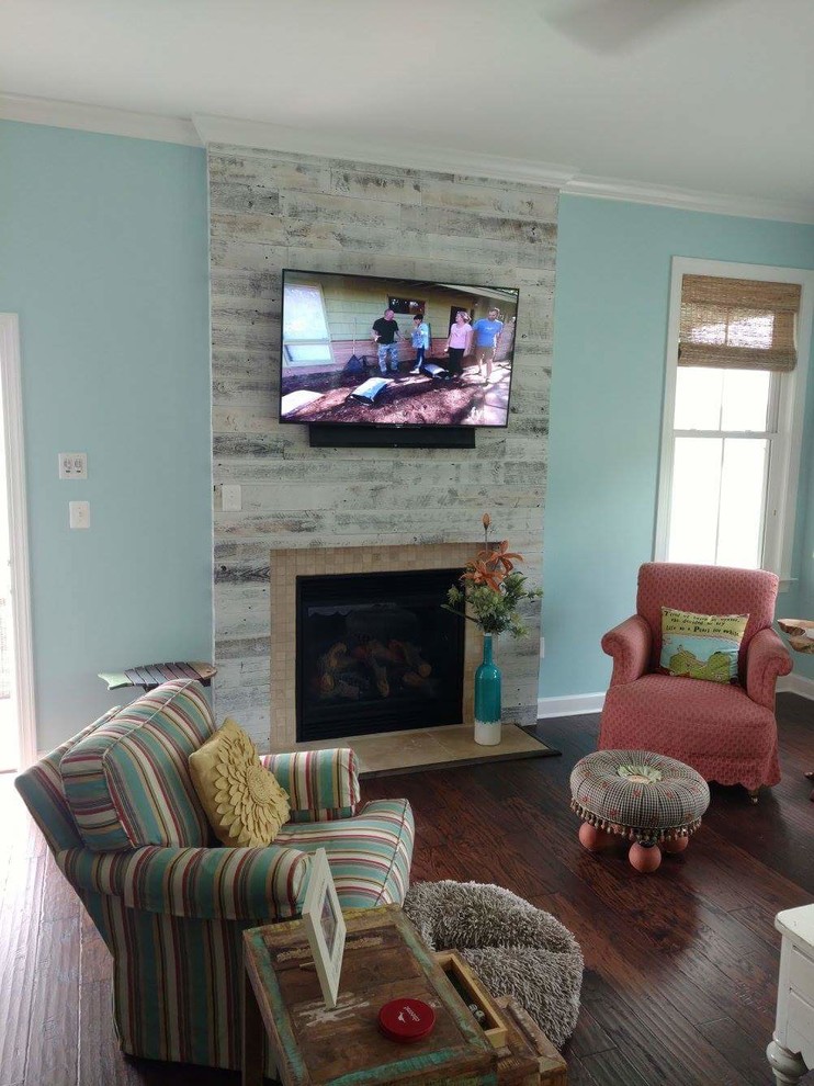 他の地域にある低価格の中くらいなビーチスタイルのおしゃれなLDK (青い壁、濃色無垢フローリング、標準型暖炉、タイルの暖炉まわり、壁掛け型テレビ、茶色い床) の写真