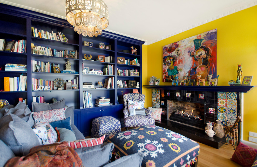 На фото: большая изолированная гостиная комната в стиле фьюжн с с книжными шкафами и полками, желтыми стенами, паркетным полом среднего тона, стандартным камином и фасадом камина из плитки с