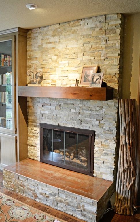 Cette image montre un salon design avec une bibliothèque ou un coin lecture, un mur beige, un sol en bois brun, une cheminée standard et un manteau de cheminée en pierre.